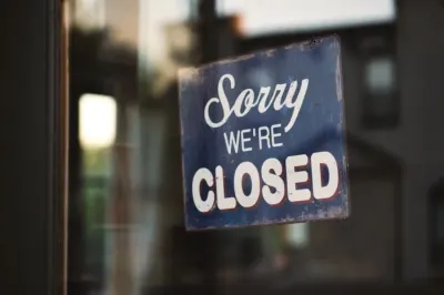 A weathered 'Sorry we're closed' sign hanging in a shop window, illustrating the effect of shutting down the economy