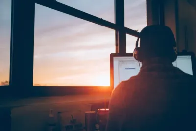 Silhouette of a person wearing headphones working at a desk as the sun sets, illustrating a post-pandemic power shift