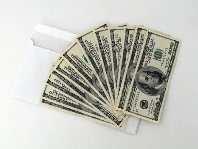 Fanned stack of hundred-dollar notes emerging from a white envelope, referencing donations to anti-climate politicians