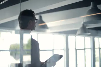 Businessman in a glass walled office holding a tablet, illustrating ethical transgressions in consulting