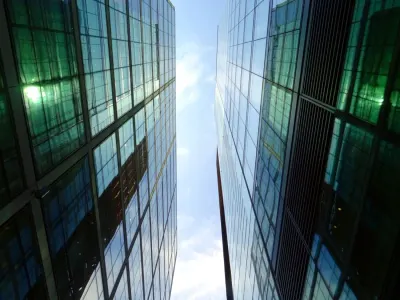 Upward view between two glass skyscrapers against a blue sky, reflecting advances in real estate tech