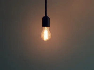A single light bulb glowing in a dim room, illustrating rising business energy costs
