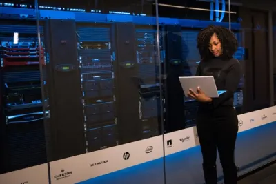 A businesswoman checking a laptop in front of server racks in a data centre, reflecting the push for IT agility
