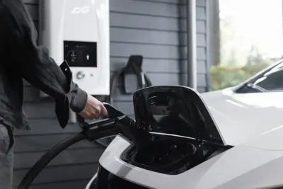 A person plugging a charging cable into an electric car outside a house, illustrating growing EV adoption