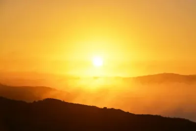 Sun glowing through haze over dark hills, illustrating the impact of heat waves on trade