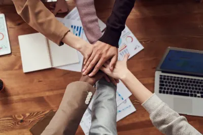 Diverse group of hands stacked together over charts and a laptop, illustrating DEI hiring practices