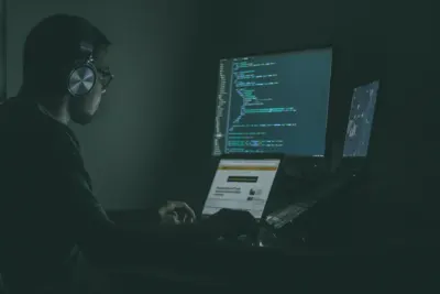 A man wearing headphones working late at multiple computer screens, illustrating cybersecurity challenges