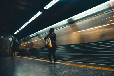 A commuter waiting on a platform as a train speeds past in a blur, illustrating the return of the morning commute