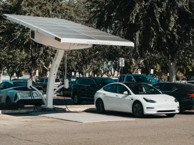 Solar-panelled EV charging canopy above a white electric car in a car park, illustrating the EV rollout