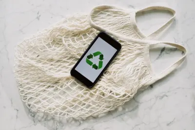 A smartphone showing a recycling symbol resting on a reusable mesh bag, illustrating sustainability messaging