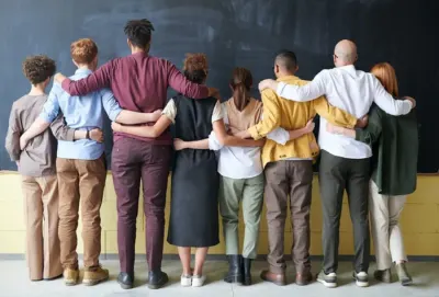 Diverse group of people standing arm in arm facing a blackboard, illustrating diversity and inclusion initiatives