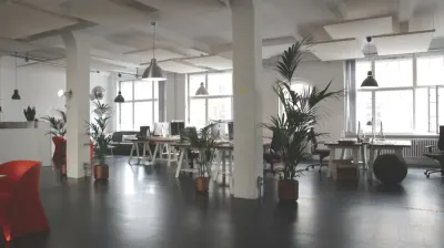 An empty open-plan office with desks, chairs and potted plants, reflecting reduced office space needs
