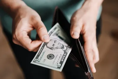 Hands pulling a five-dollar note from a wallet, illustrating living paycheck to paycheck