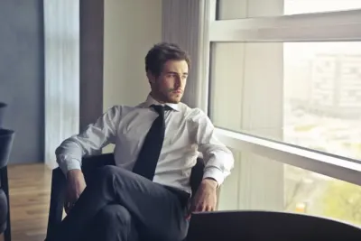 Man in shirt and tie sitting by an office window looking out pensively, illustrating white-collar staff shortages
