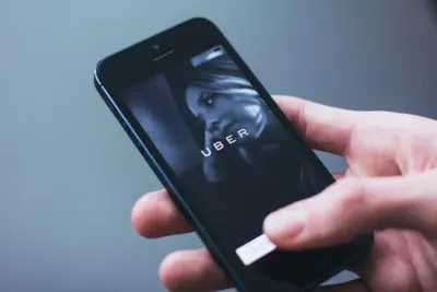 Hand holding a smartphone displaying the Uber app, referencing the Brussels Court of Appeal ruling on UberX drivers