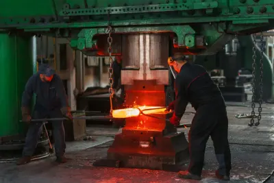 Factory workers forging a glowing hot metal bar with a large press, illustrating manufacturing skills shortages