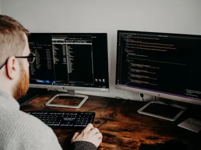A developer reviewing code across dual monitors at a wooden desk, from a study on the best sectors to invest in