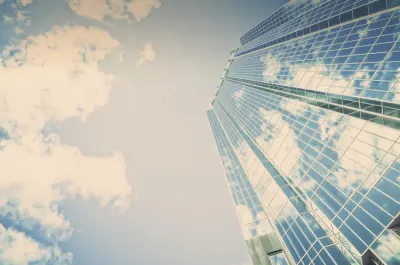 Low angle view of a glass office tower against a cloudy sky, symbolising organisational transformation