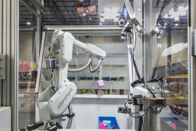 White robotic arm sorting items inside a glass-walled warehouse cell, illustrating warehouse automation robots