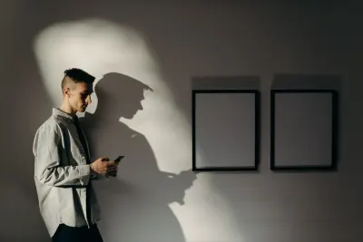 Man checking his phone alone in a room beside two empty picture frames, evoking remote work isolation