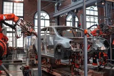 Orange robotic arm welding a car body on a factory production line, illustrating robot investment