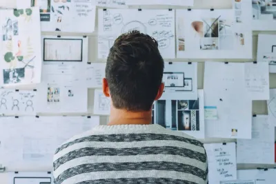 Man viewed from behind studying a wall covered in notes, sketches and photos, illustrating a four step plan to adapt workforce strategies post-Covid