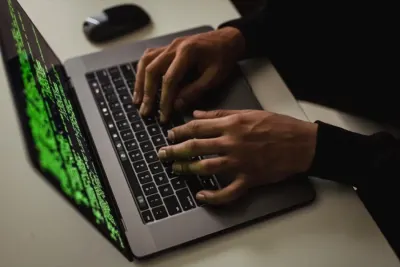 Hands typing on a laptop with green code cascading on screen, illustrating weekly ransomware attacks