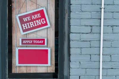 A 'We Are Hiring, Apply Today' sign in a shop window, reflecting the gap between young talent and employers