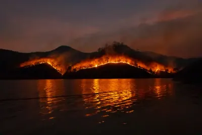 Wildfire glowing across a hillside beside a lake at dusk, underscoring the climate crisis and a transformative mindset