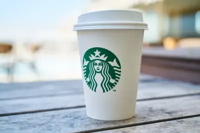 A takeaway coffee cup with a familiar green logo on an outdoor table, illustrating brand loyalty