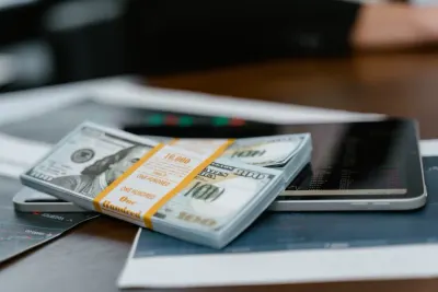 A bundled stack of hundred dollar bills resting on financial charts and a tablet, reflecting rising IT spending
