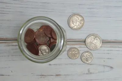 A glass jar of coins beside loose US quarters and dimes on a wooden surface, illustrating rising insolvencies
