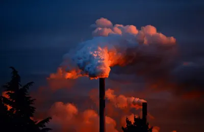 Industrial chimney billowing smoke against a fiery sunset sky, illustrating carbon pricing and the energy transition