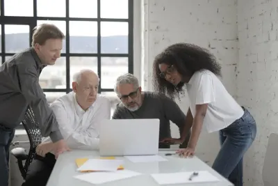 Four colleagues of mixed ages and backgrounds gathered around a laptop in a bright office, illustrating debate over gender quotas