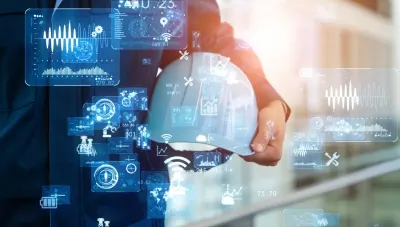 An engineer holding a hard hat surrounded by digital data overlays, representing building management systems